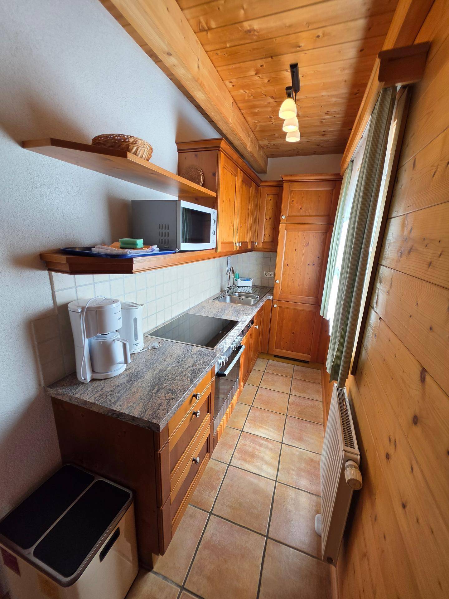 Schmale Küche mit Holzschränken, Granitarbeitsplatte, Induktionskochfeld und Mikrowelle, gefliestem Boden.