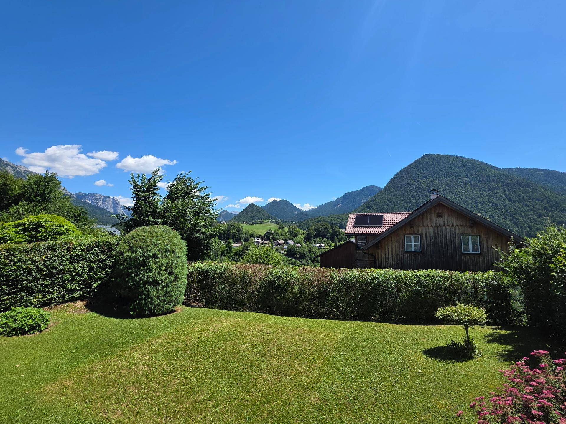 Weitläufiger Garten mit Rasen und Hecken, umgeben von einer beeindruckenden Bergkulisse.