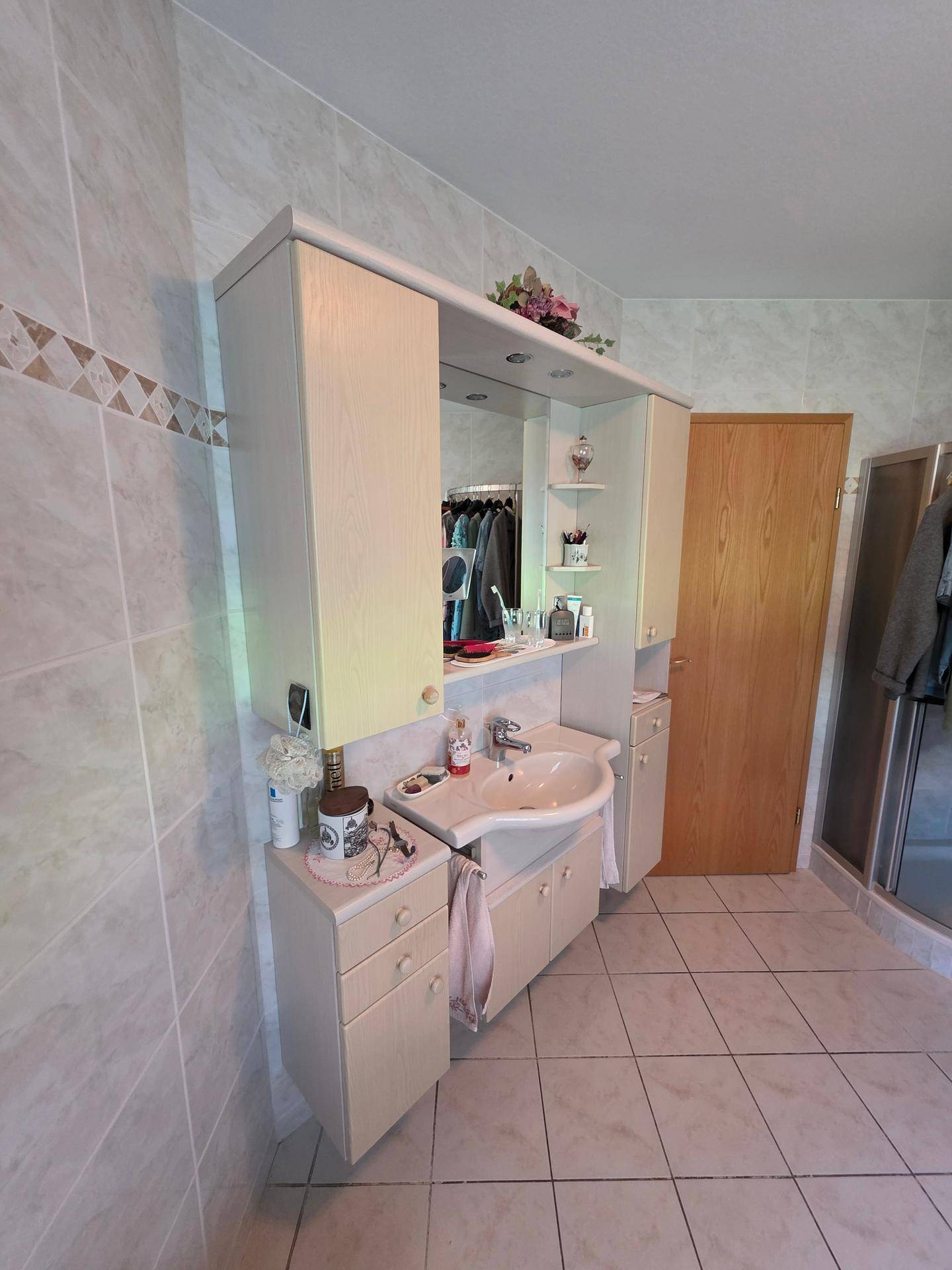 Funktionales Badezimmer mit Einzelwaschbecken, Spiegelschrank und hellen Fliesen an Wänden und Boden.