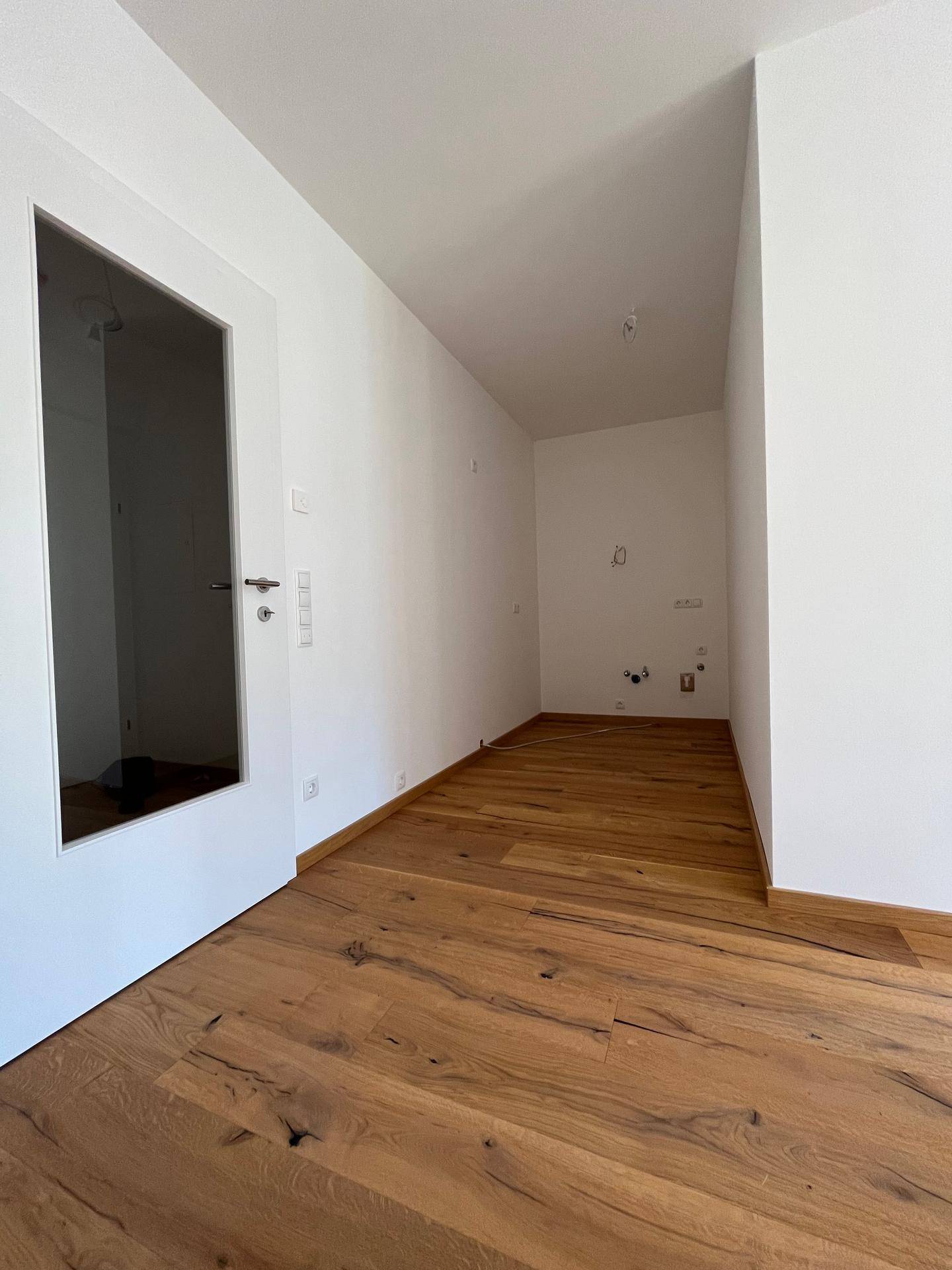 Funktionaler Raum mit Holzboden und vorbereiteten Anschlüssen, ideal als Hauswirtschaftsraum oder kleine Küche.