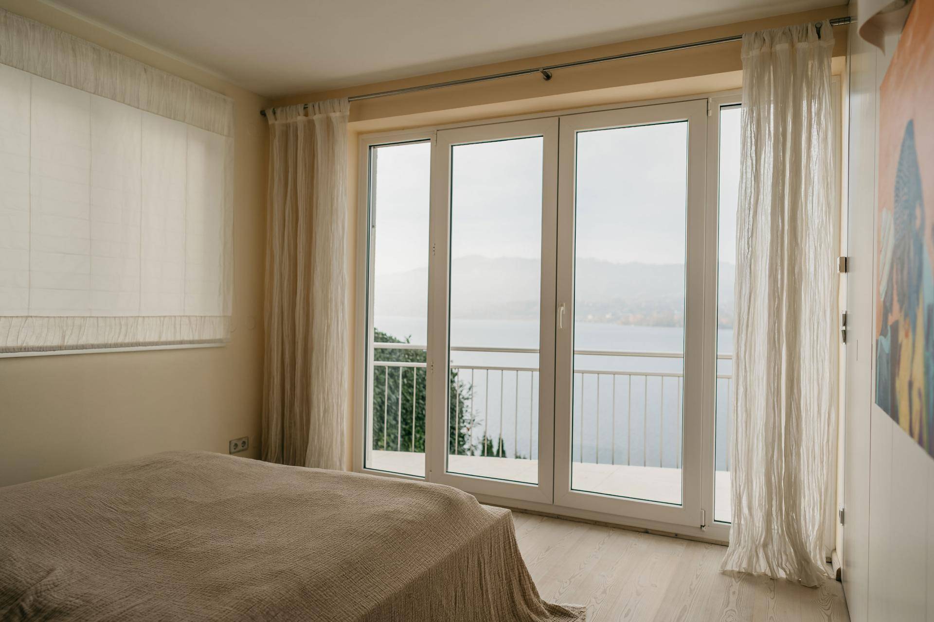 Helles Schlafzimmer mit Seeblick, Balkonzugang und hellem Holzboden.
