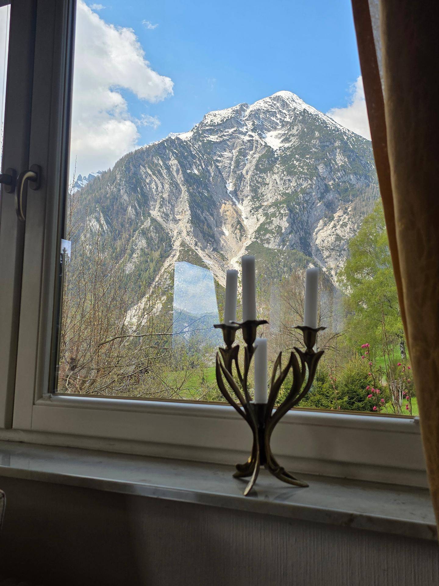 Spektakulärer Bergblick durch ein Fenster, mit schneebedeckten Gipfeln und grüner Landschaft.