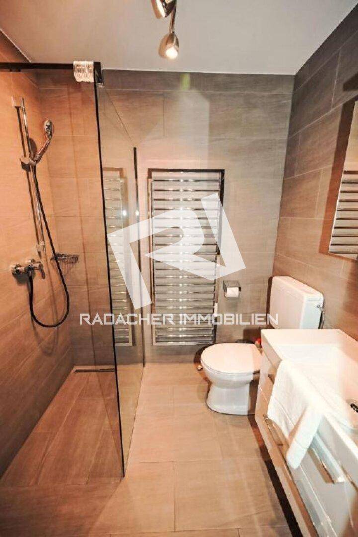 Helles Badezimmer mit ebenerdiger Dusche, WC, Waschbecken und beheiztem Handtuchhalter in modernem Design.