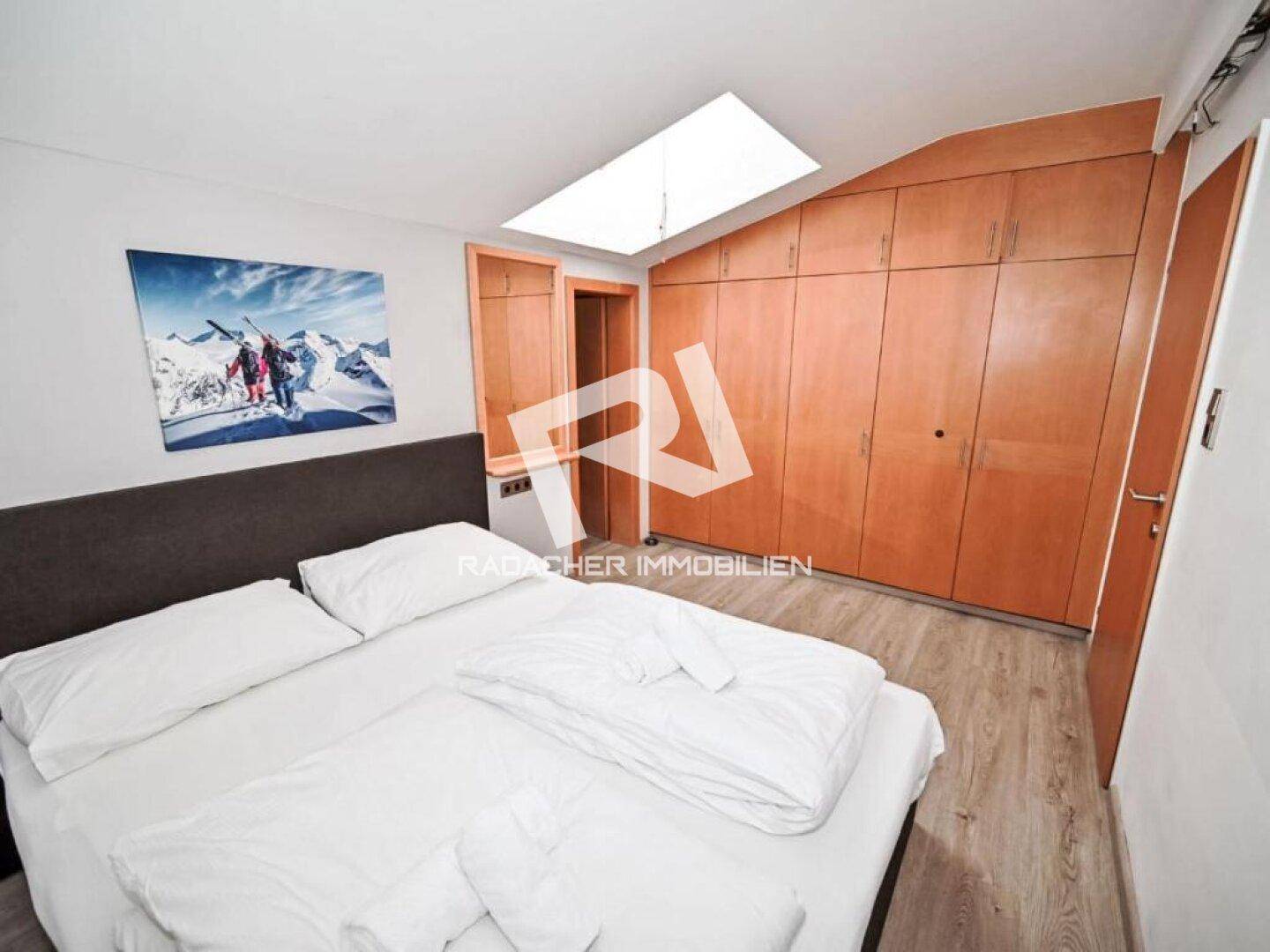 Gemütliches Schlafzimmer mit Doppelbett, Einbauschränken aus Holz und einem Dachfenster für Helligkeit.
