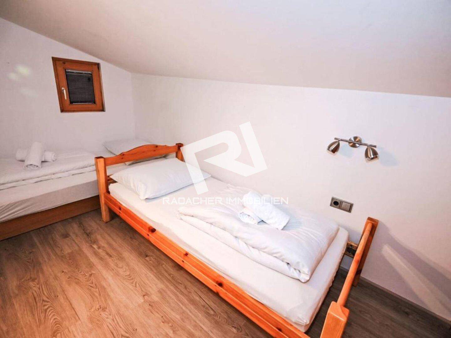 Helles Schlafzimmer mit zwei Einzelbetten, kleinem Fenster und Dachschräge, ideal als Gästezimmer.