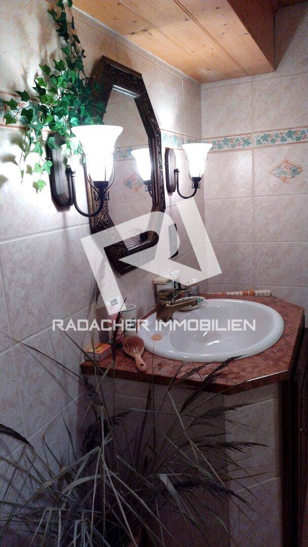 Badezimmer mit traditionellem Waschbecken, Spiegel und Wandleuchten, gefliest in hellen Tönen.
