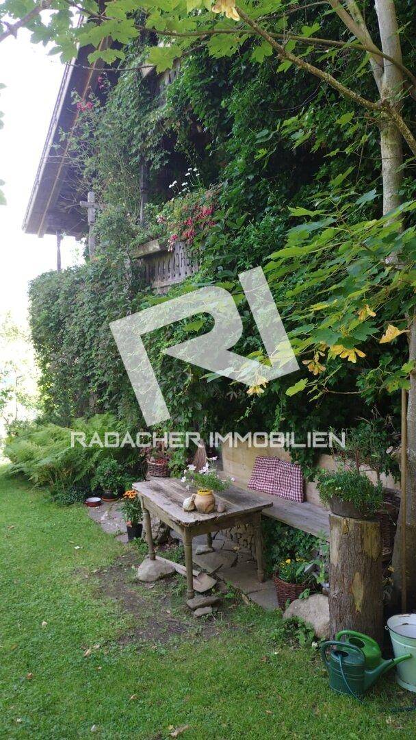 Gemütlicher Sitzbereich im Garten mit rustikalem Holztisch und Bank, umgeben von üppiger Vegetation.