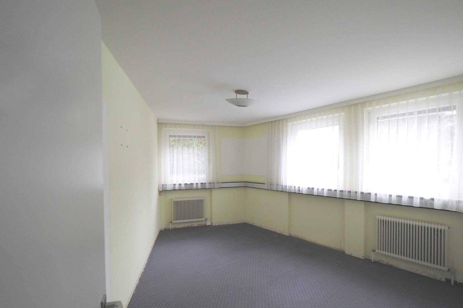 Helles Zimmer mit drei Fenstern, Teppichboden und Heizkörpern, bereit zur individuellen Gestaltung.