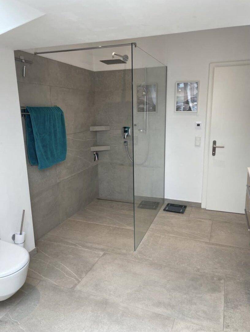 Geräumige begehbare Dusche mit Glasabtrennung, Regendusche und modernen grauen Fliesen.