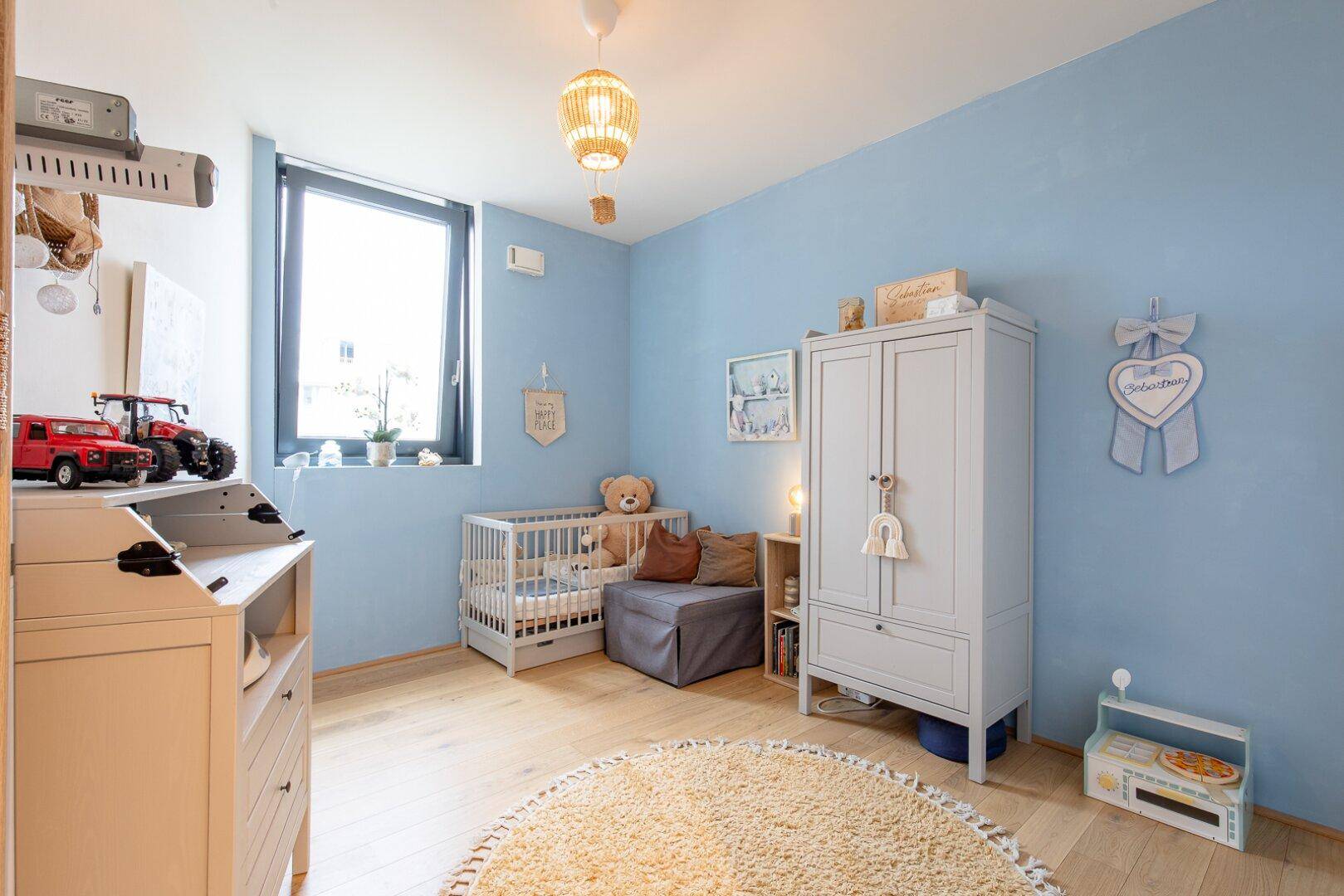 Helles Kinderzimmer mit hellblauen Wänden, Holzboden, Babybett und Kleiderschrank.
