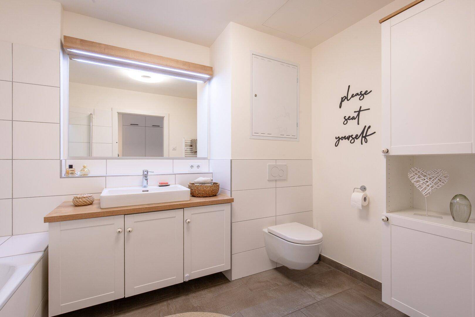 Modernes Badezimmer mit weißen Fliesen, Einzelwaschbecken, Holzplatte und wandhängendem WC.
