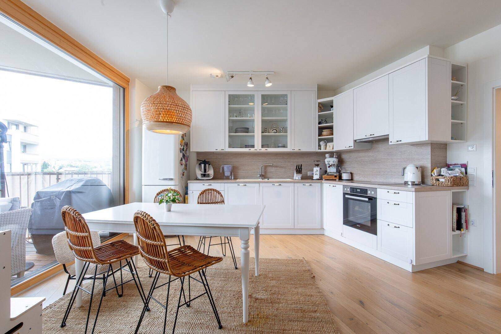 Helle, moderne Küche mit weißen Schränken, Holzboden und Essbereich mit Zugang zum Balkon.