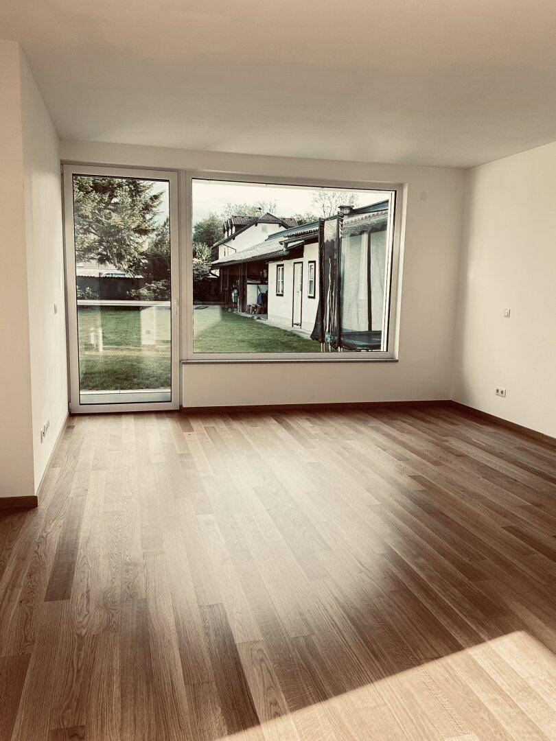 Heller Wohnraum mit Holzboden und großen Fenstern mit Blick auf den Garten.