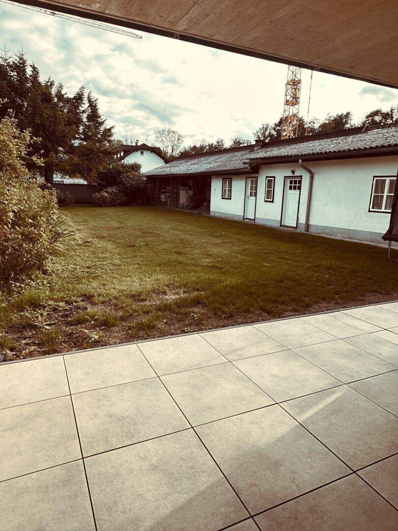 Große geflieste Terrasse mit Blick auf eine weitläufige Rasenfläche und ein traditionelles Haus.