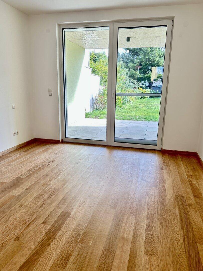 Geräumiger Raum mit Holzboden und großer Glastür, die zur Terrasse führt.