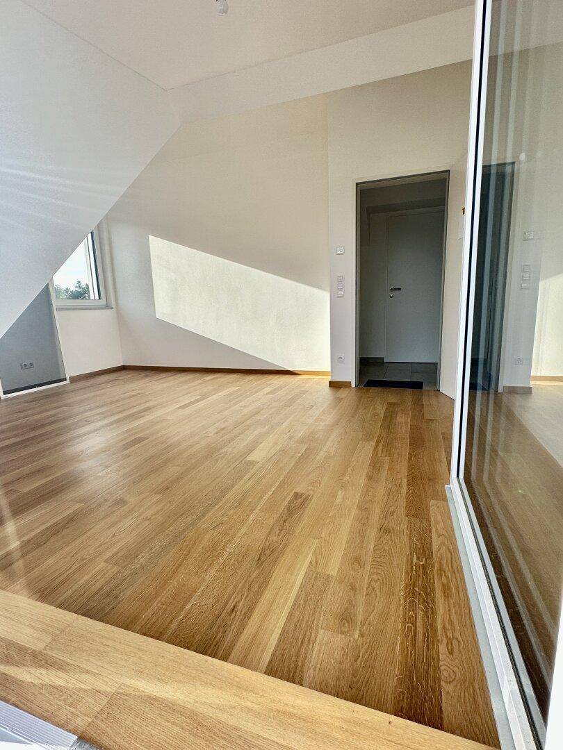 Heller Raum mit Holzboden, Dachschräge und viel natürlichem Licht.