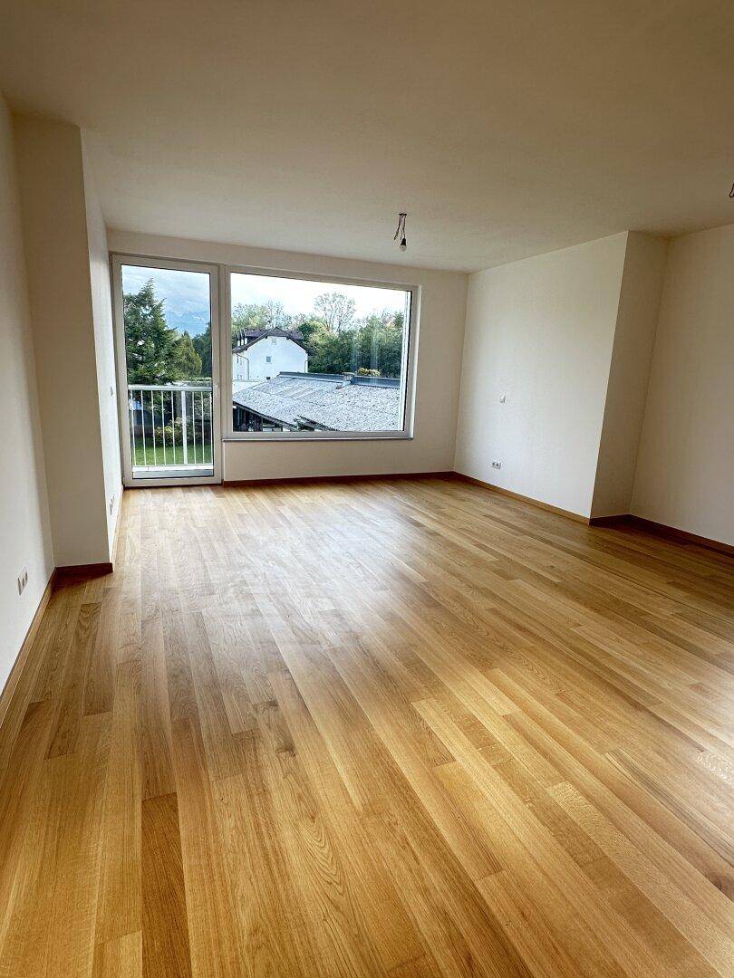 Heller Wohnraum mit großen Fenstern, Holzboden und Zugang zu einem Außenbereich mit grüner Aussicht.