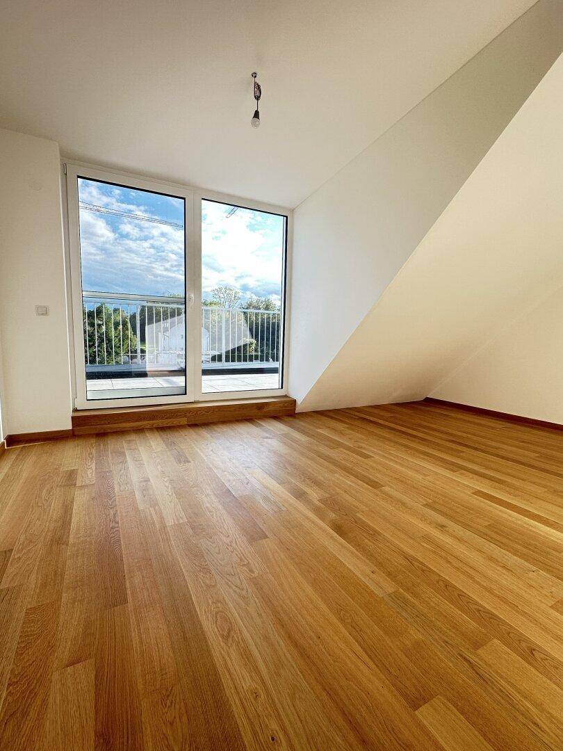 Lichtdurchfluteter Raum mit Holzboden, großen Fenstern und schräger Decke, ideal als Schlaf- oder Wohnzimmer.