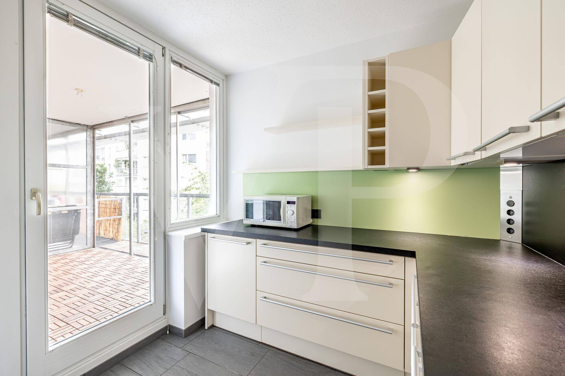 Moderne Küche mit hellen Schränken, dunkler Arbeitsplatte und Zugang zur Loggia.