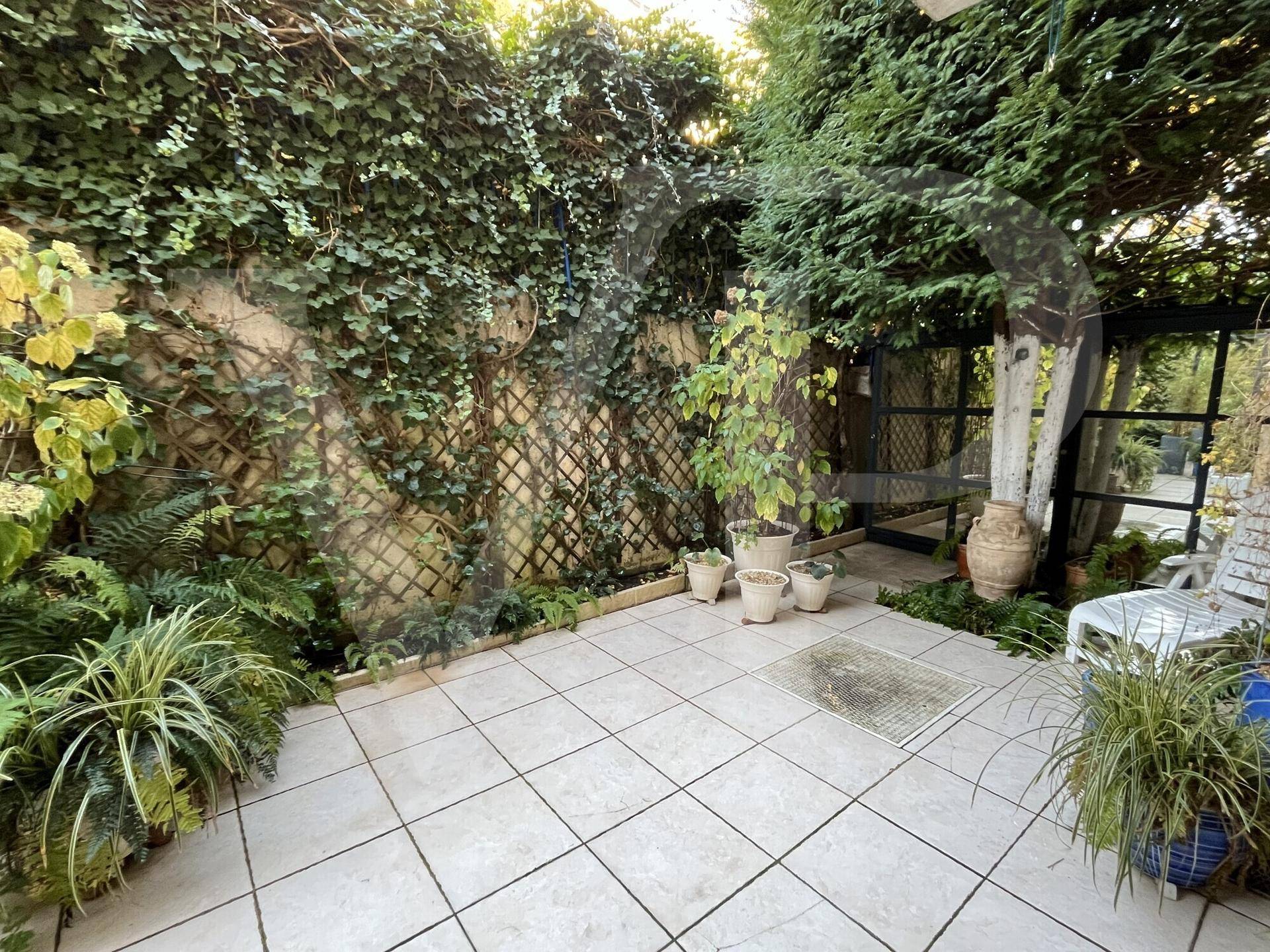 Geflieste Terrasse mit Kletterpflanzen an der Wand und Topfpflanzen, umgeben von viel Grün.