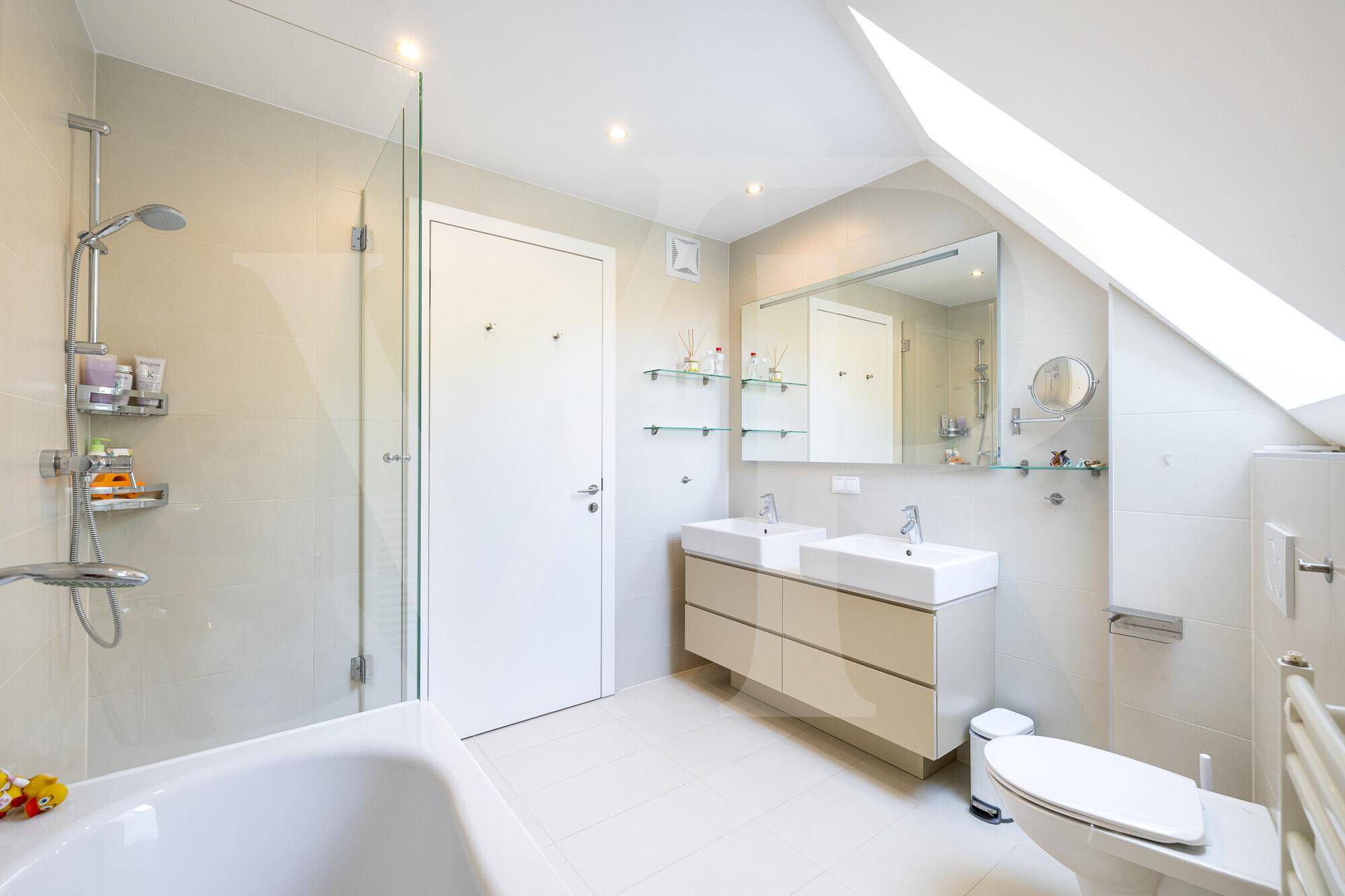 Geräumiges Badezimmer mit Doppelwaschbecken, Badewanne, Dusche und Dachschräge für natürliches Licht.