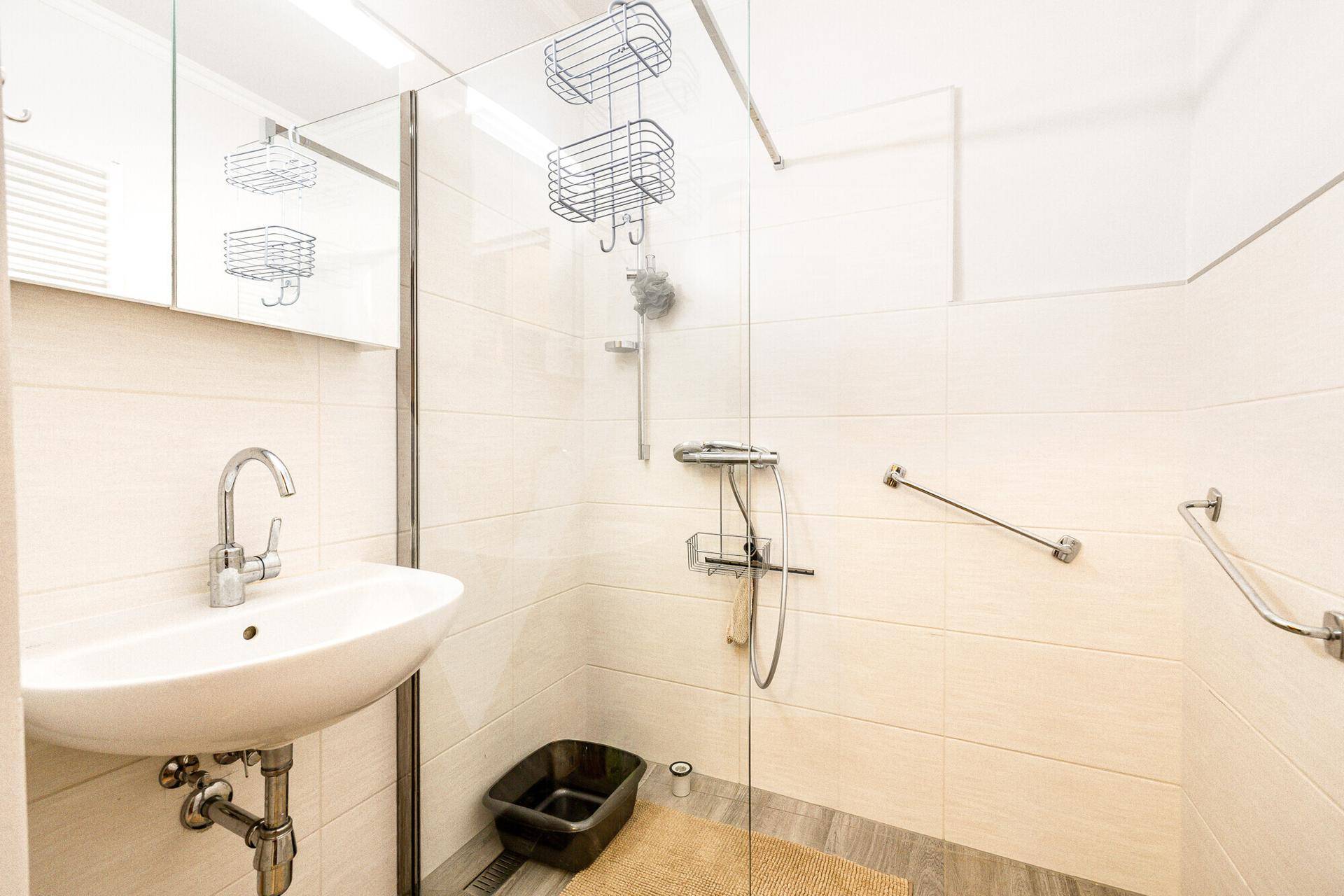 Modernes Badezimmer mit ebenerdiger Dusche, Waschbecken und weißen Fliesen.
