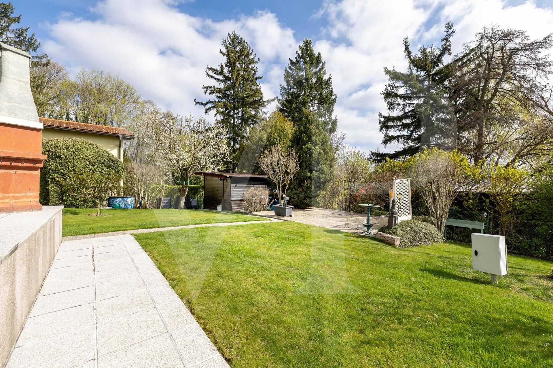 Gepflegter Gartenbereich mit Rasenfläche, gepflastertem Weg und Gartenhaus.