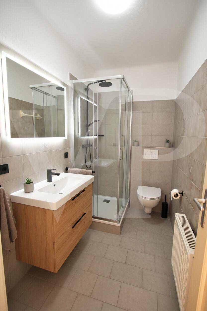 Modernisiertes Badezimmer mit grauen Fliesen, Duschkabine und beleuchtetem Spiegelschrank.