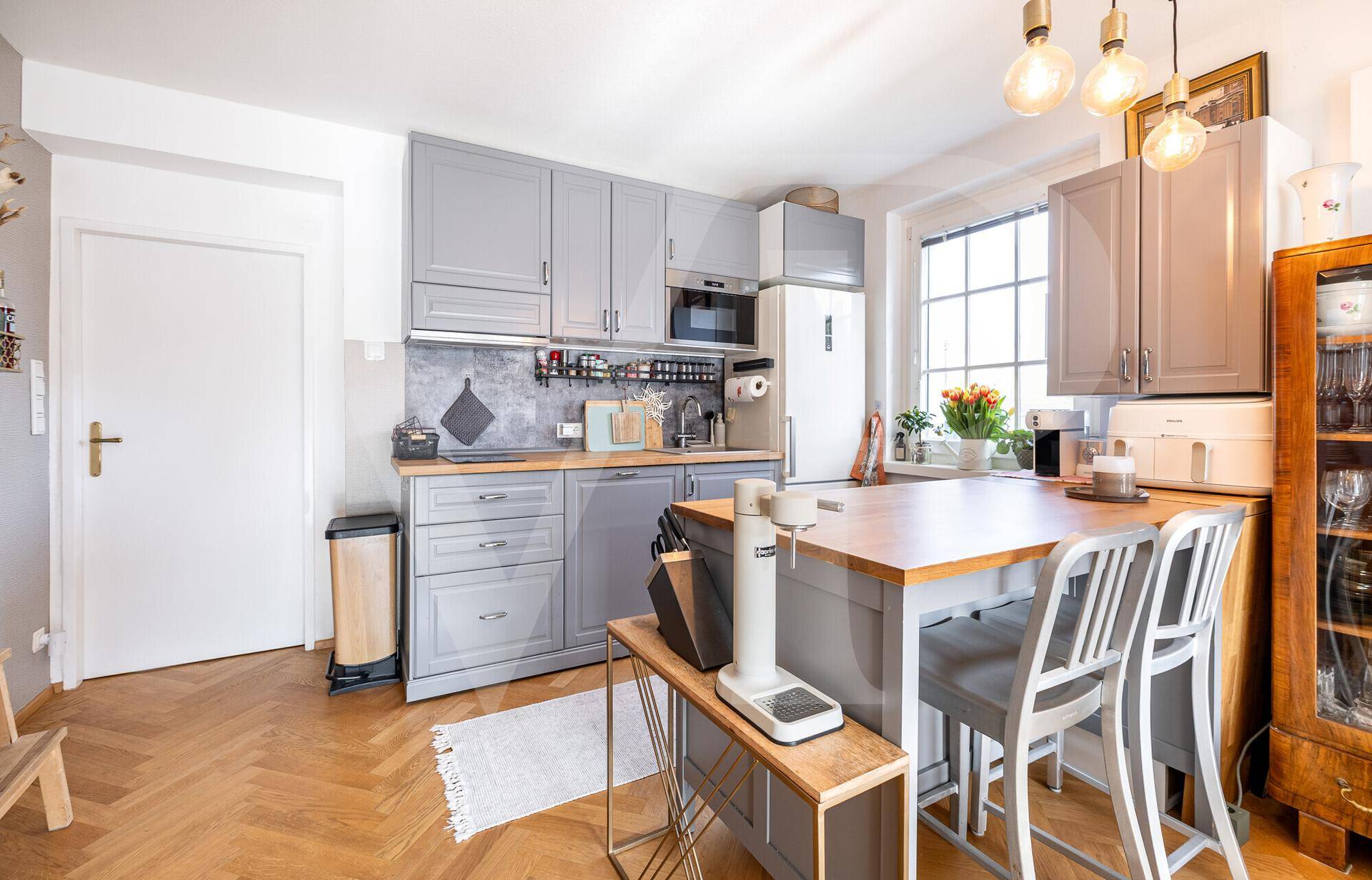 Moderne Küche mit grauen Schränken, Holztheke und integriertem Essbereich mit Barhockern.