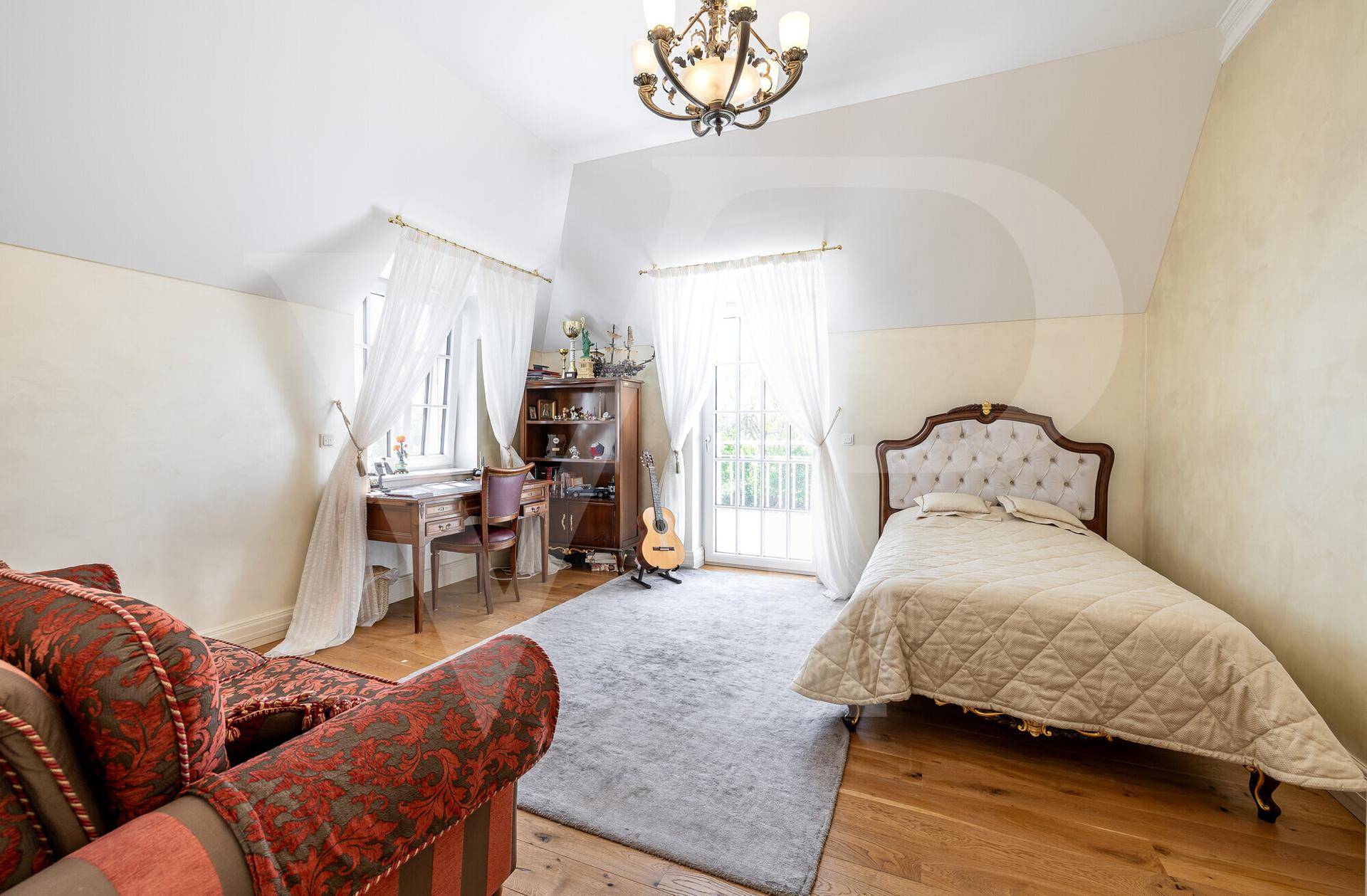 Helles Schlafzimmer mit Holzboden, Schreibtisch und Zugang zu einem französischen Balkon.