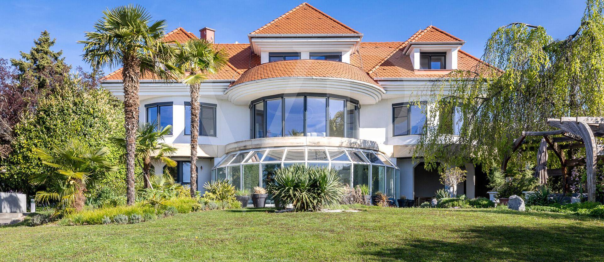 Elegante Villa mit weitläufigem Garten und mediterraner Bepflanzung unter blauem Himmel.