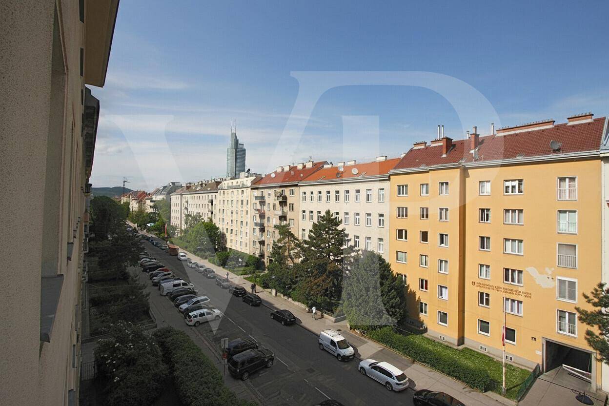 Blick von oben auf eine belebte Straße mit parkenden Autos und hohen Wohngebäuden.