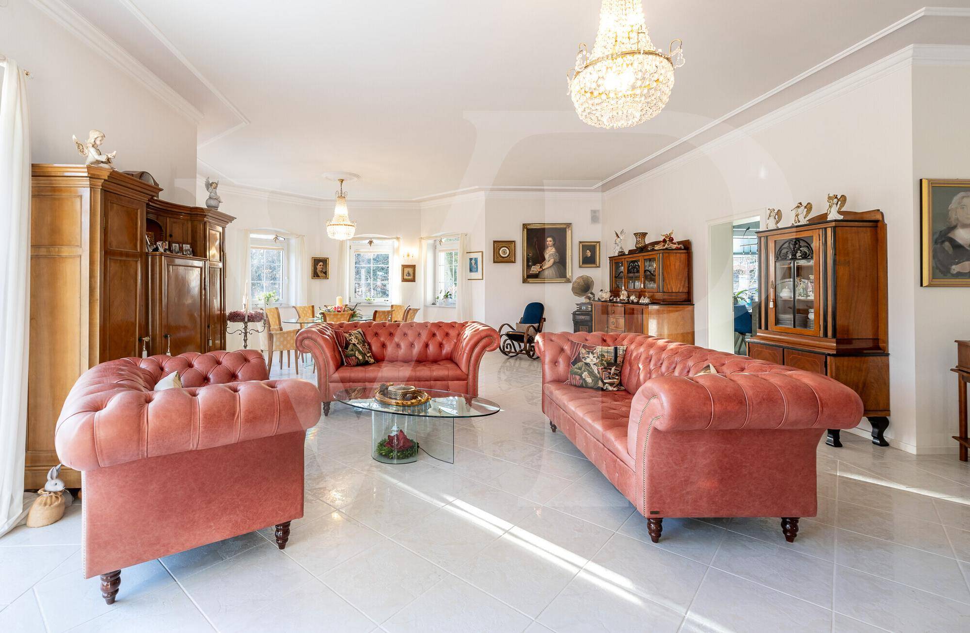 Geräumiges Wohnzimmer mit klassischen Möbeln, Kronleuchtern und hellem Fliesenboden.