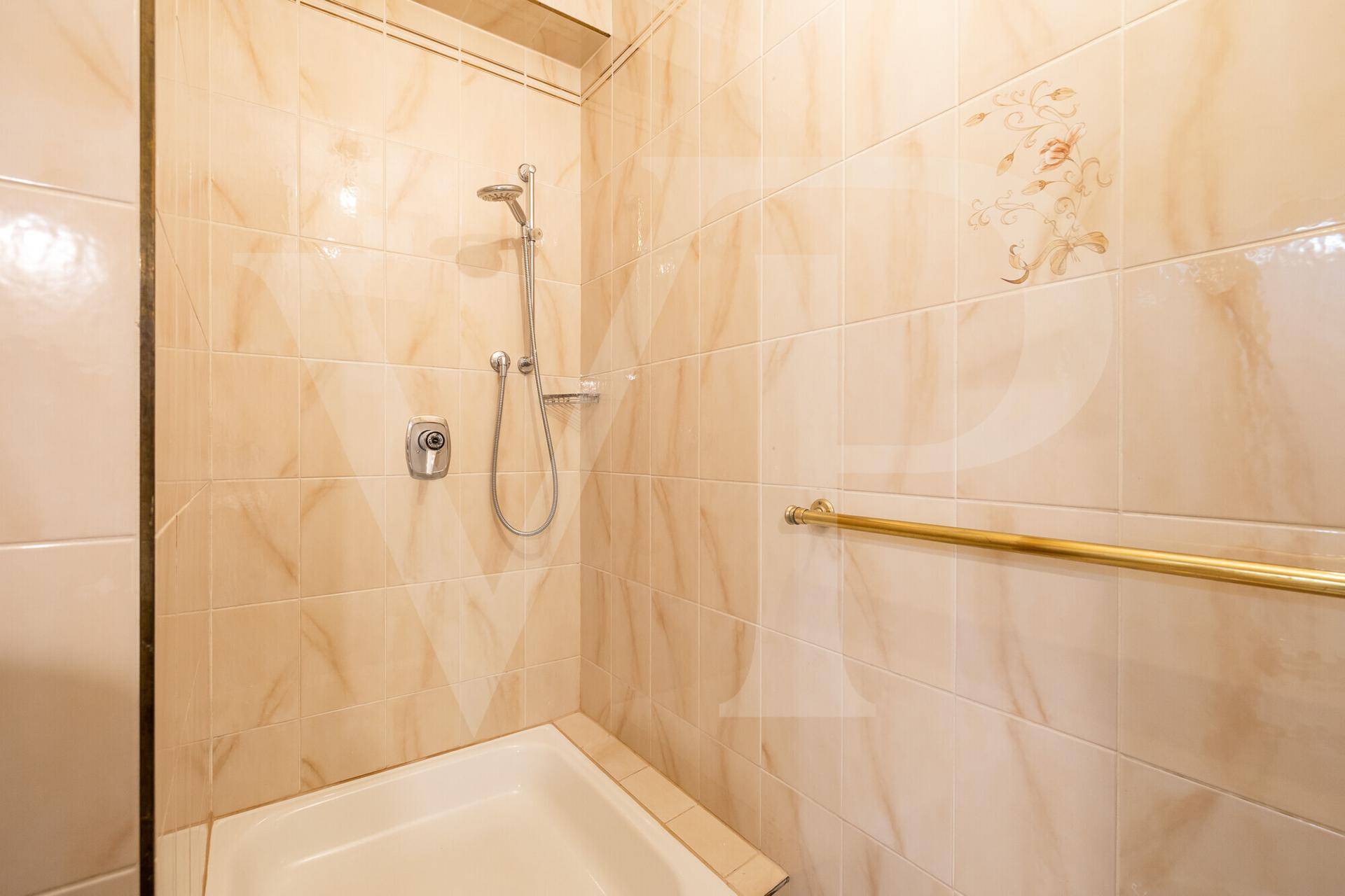 Badezimmer mit beigefarbenen Fliesen, Duschbereich und Haltegriff für Komfort.