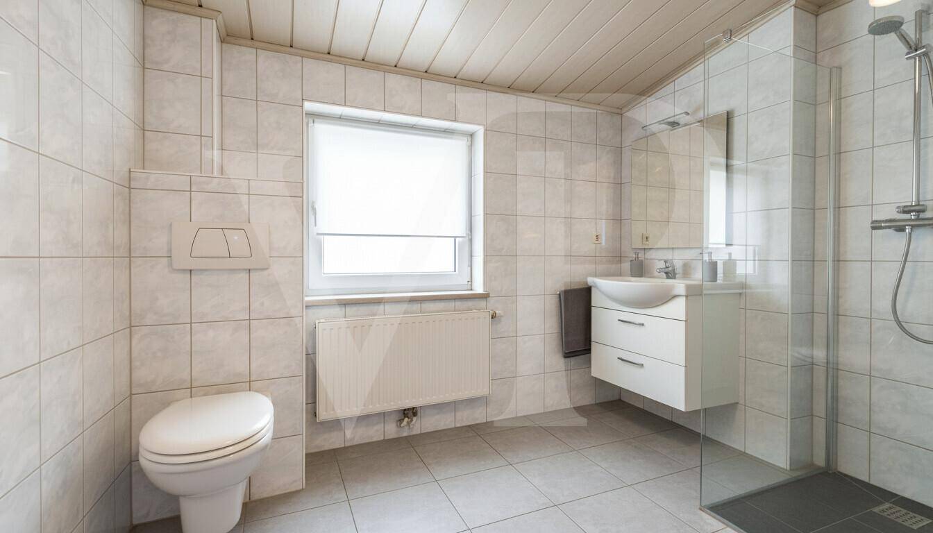 Helles Badezimmer mit weißen Fliesen, Dusche und Fenster.
