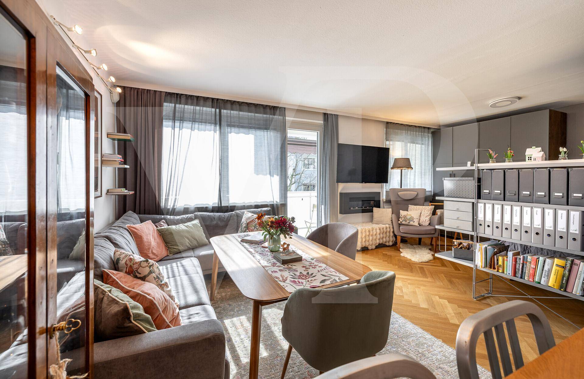Helles Wohn- und Esszimmer mit Fischgrätparkett, gemütlicher Sitzecke und Zugang zum Balkon.