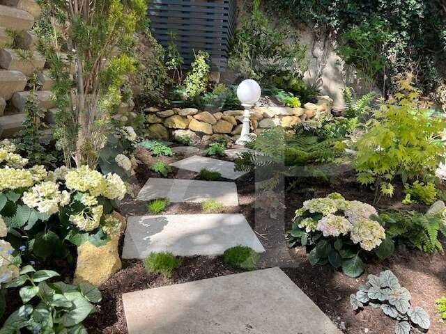 Gestufter Gartenbereich mit Steinplattenwegen, üppiger Bepflanzung und dekorativer Beleuchtung.