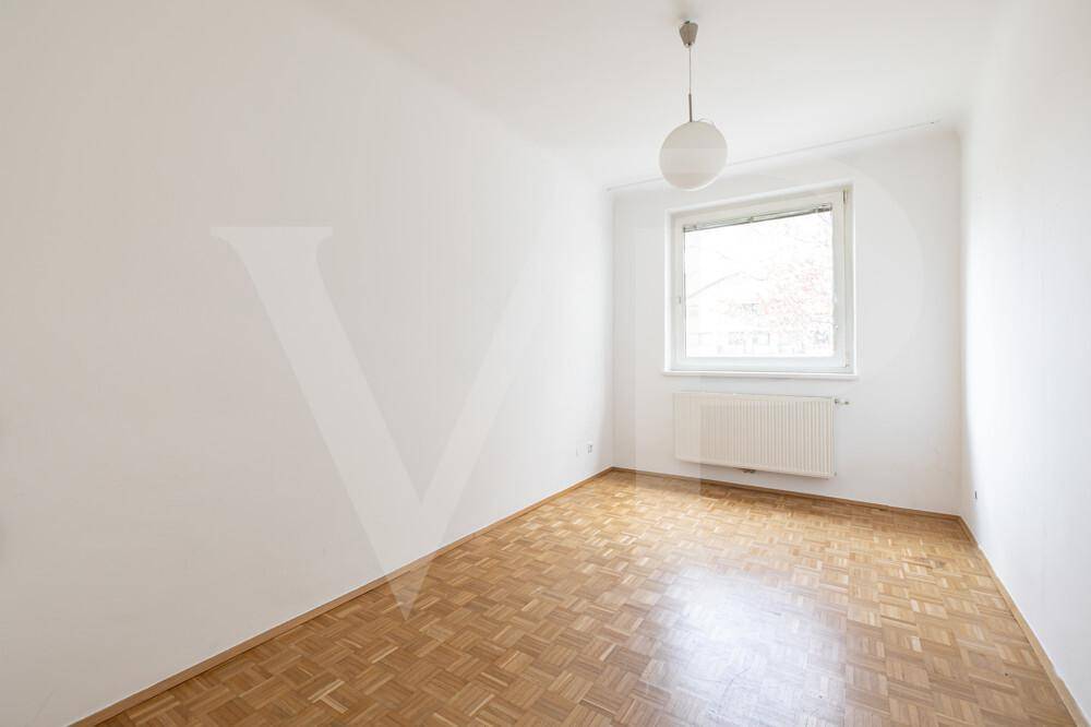 Helles Zimmer mit Parkettboden, Fenster und einfacher Deckenleuchte.