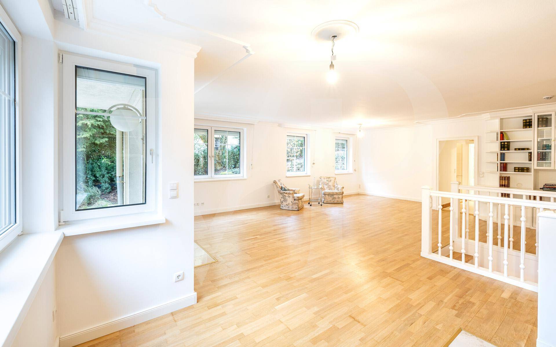 Helles Wohnzimmer mit Parkettboden, mehreren Fenstern und Blick ins Grüne.