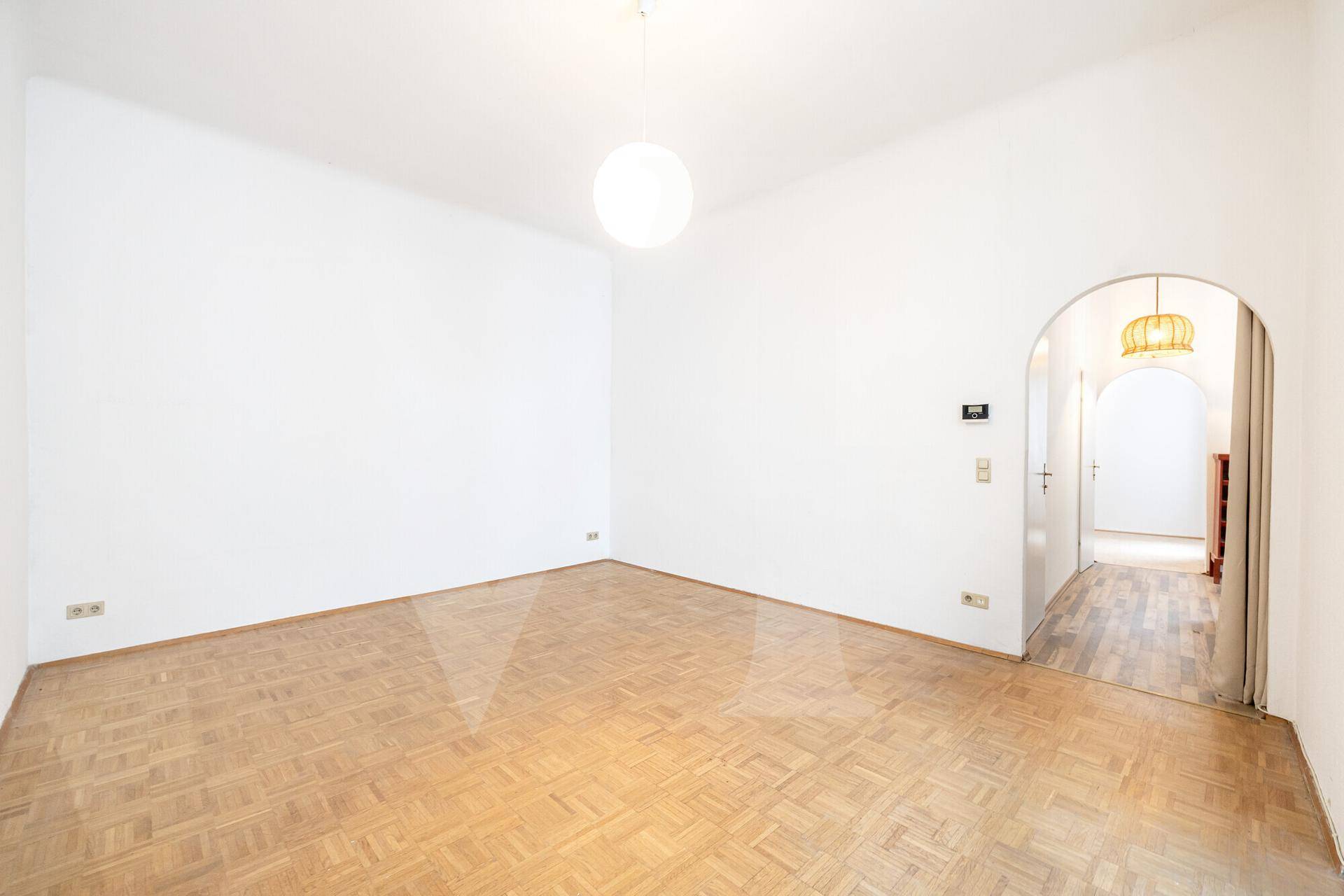 Leeres Zimmer mit Parkettboden und einem eleganten Rundbogen, der zu einem anderen Raum führt.