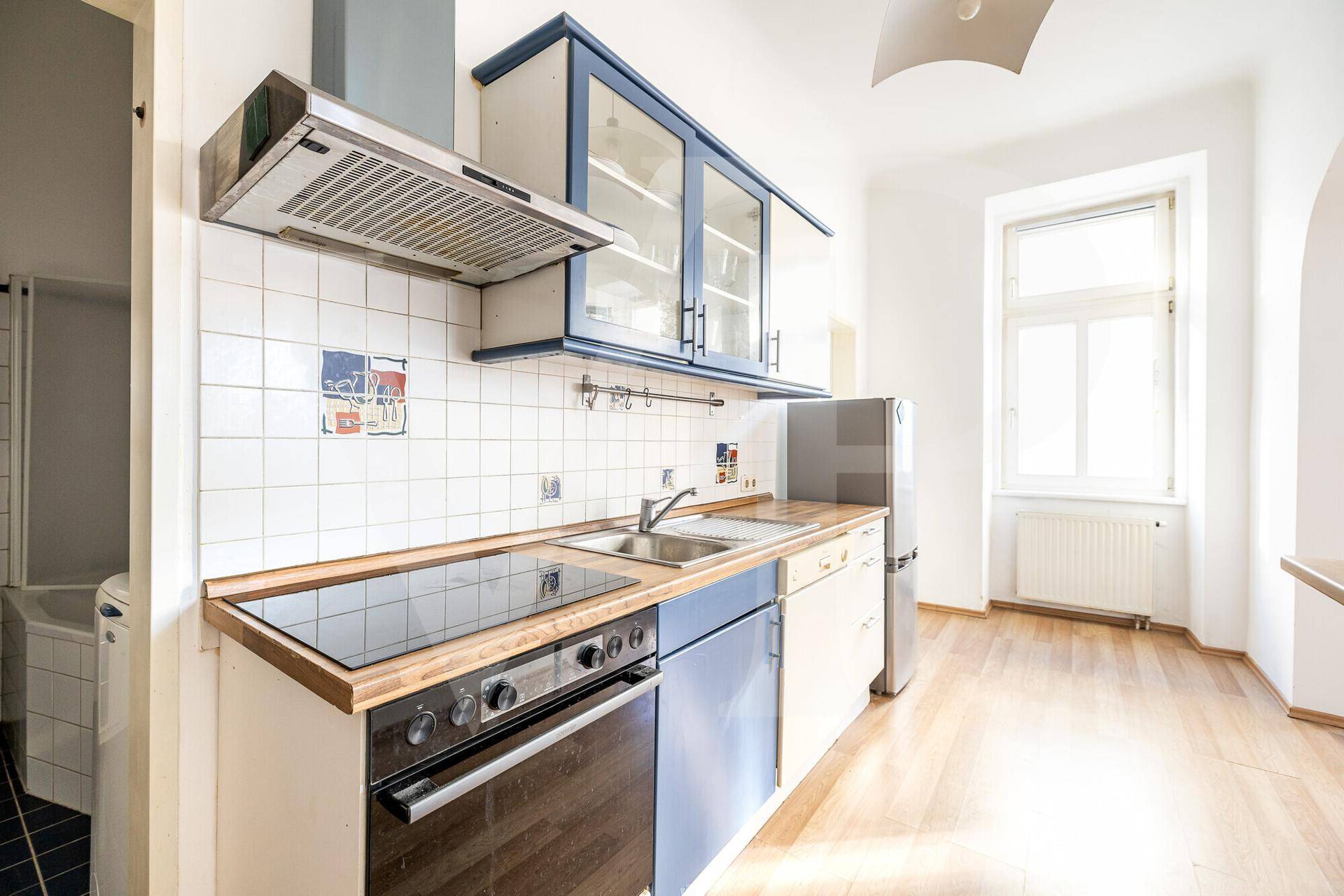 Funktionale Küche mit blauen und weißen Schränken, Fliesenrückwand und Fenster.