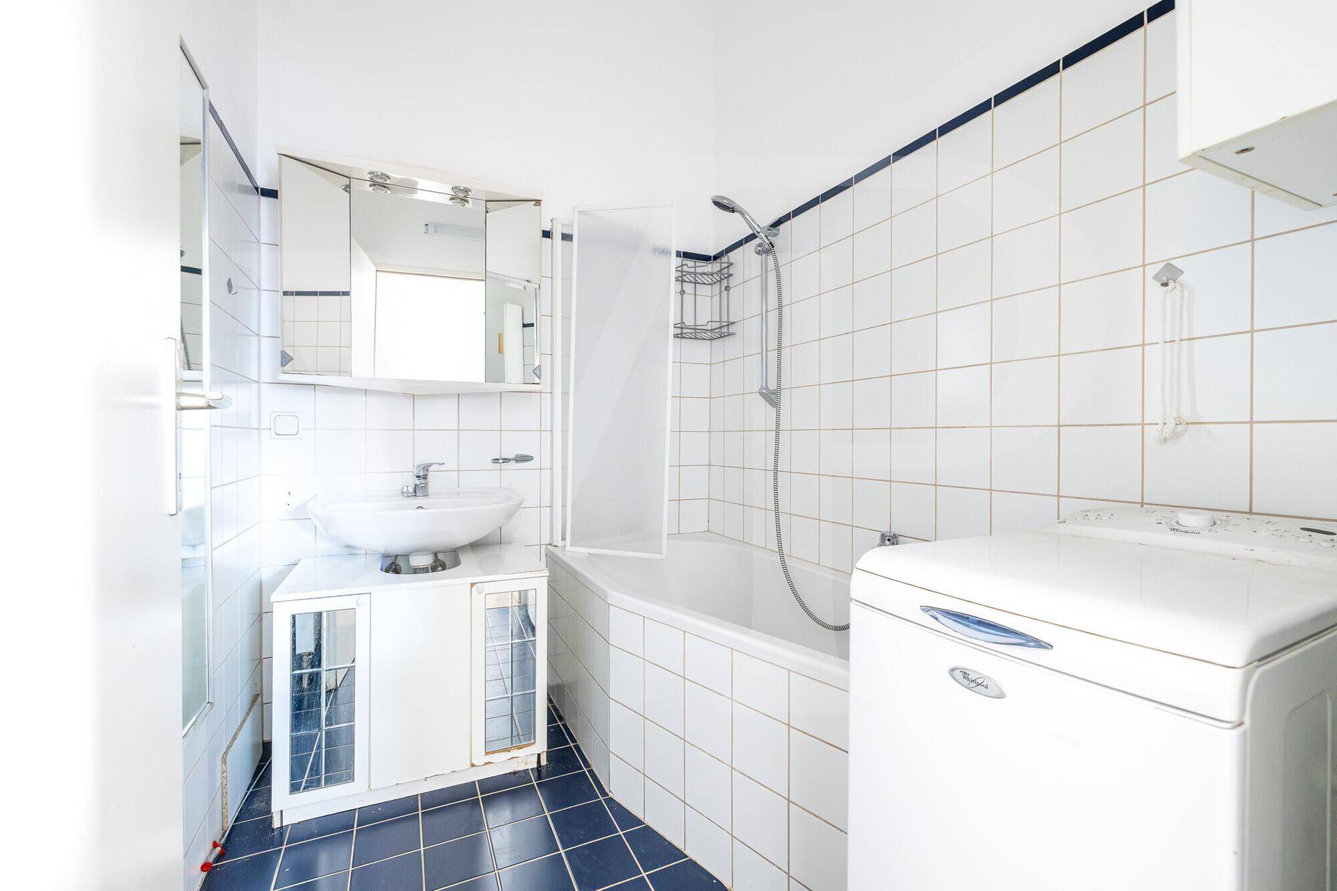 Badezimmer mit Badewanne, Dusche, Waschbecken und Waschmaschine, gefliest in Weiß und Blau.