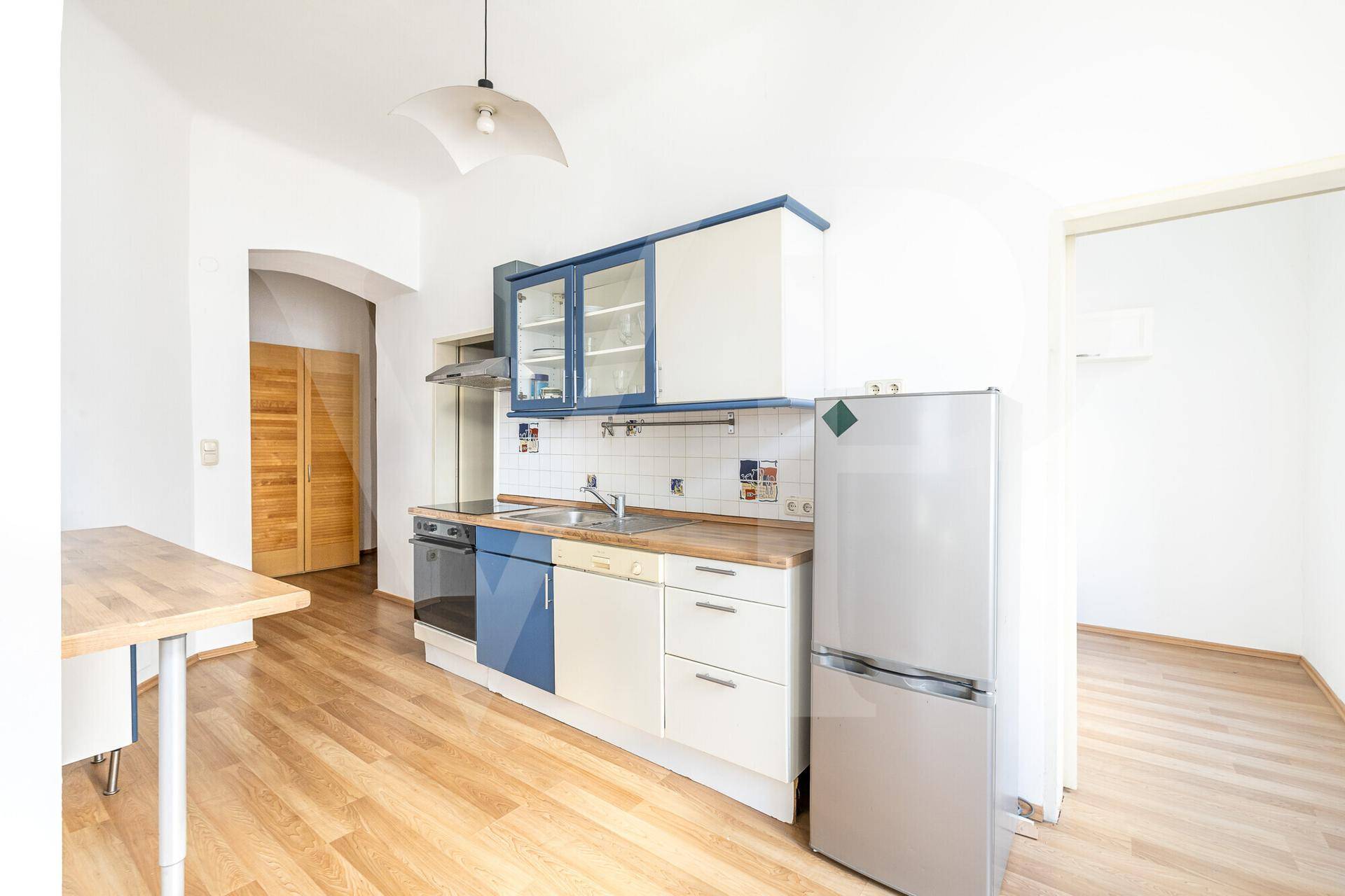 Helle Küche mit Holzboden, blauen und weißen Schränken und Kühlschrank.