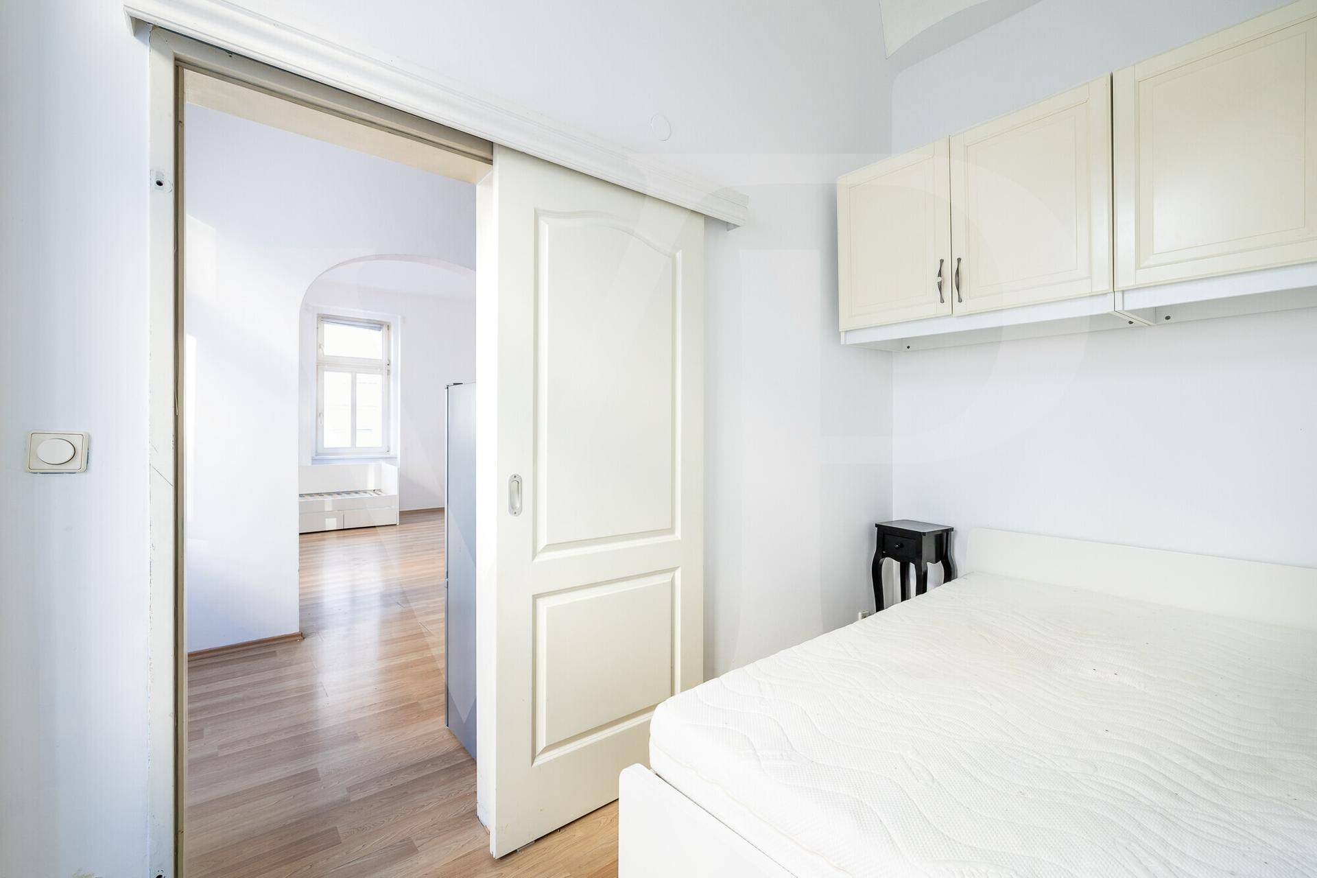 Schlafzimmer mit Schiebetür, Holzboden und praktischen Hängeschränken über dem Bett.
