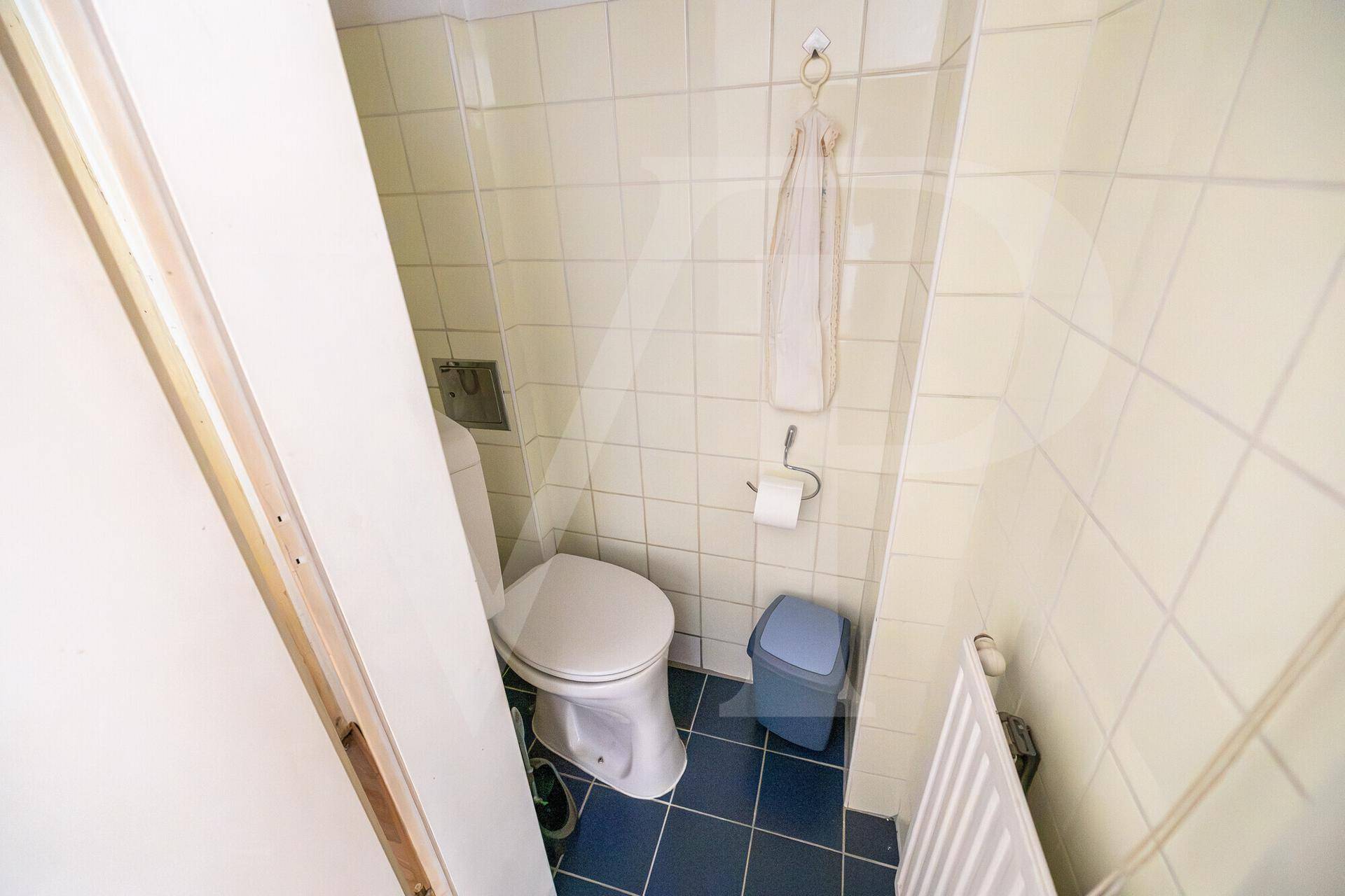 Separates WC mit Toilette und Fliesen in Hellgelb und Blau.