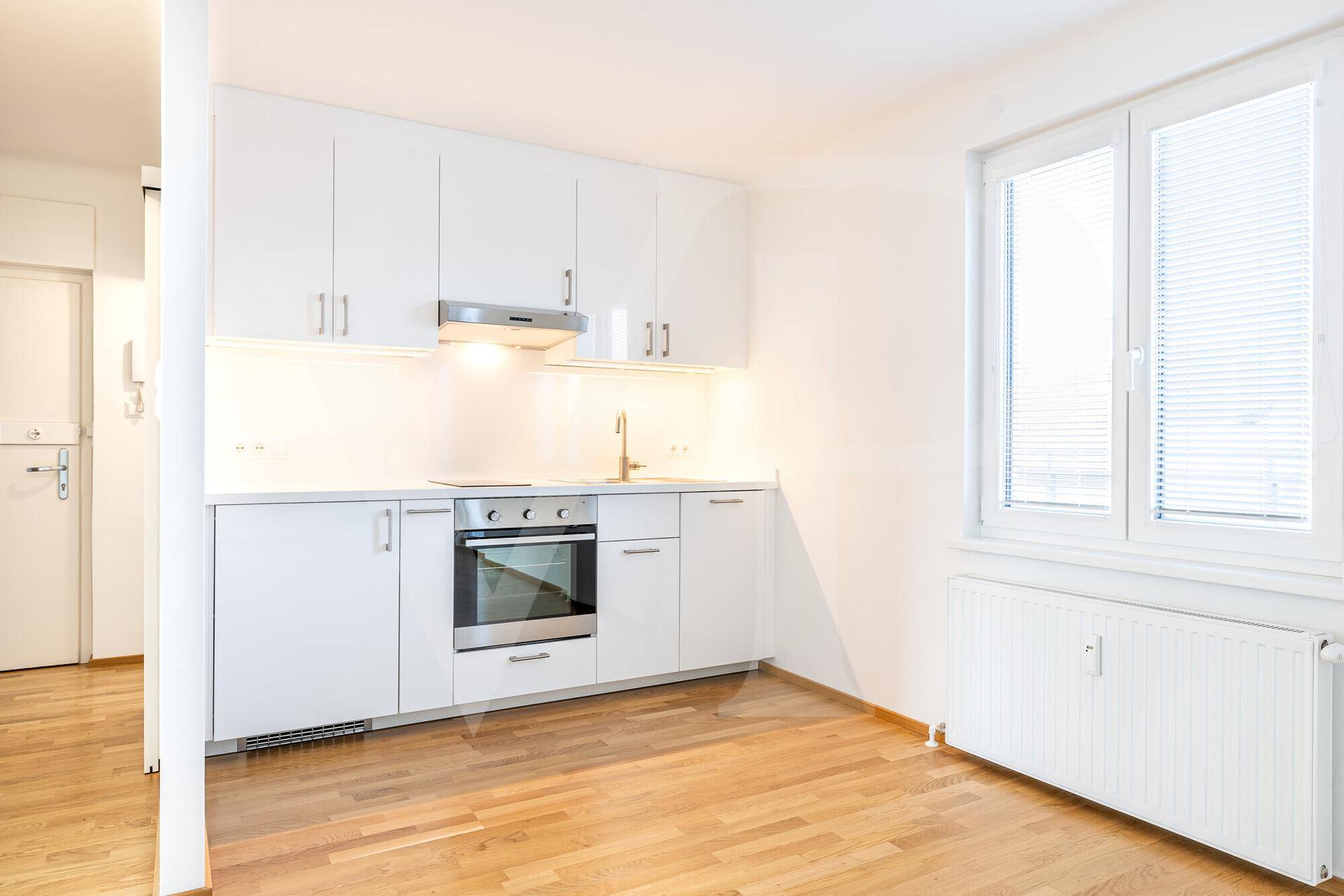 Moderne Einbauküche mit weißen Schränken, integriertem Backofen und Fenster.