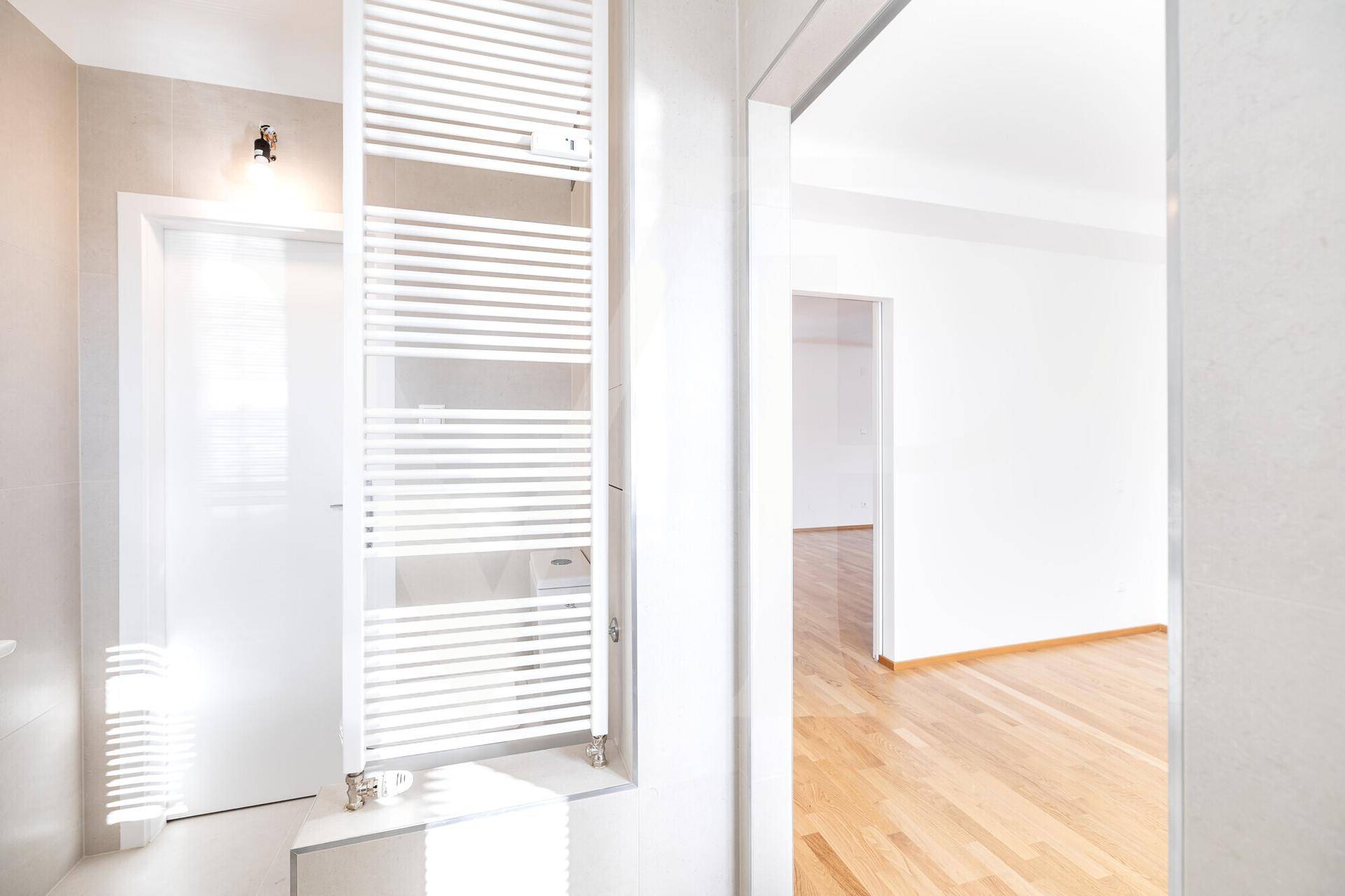 Helles Badezimmer mit Handtuchheizkörper und Blick in den angrenzenden Raum.