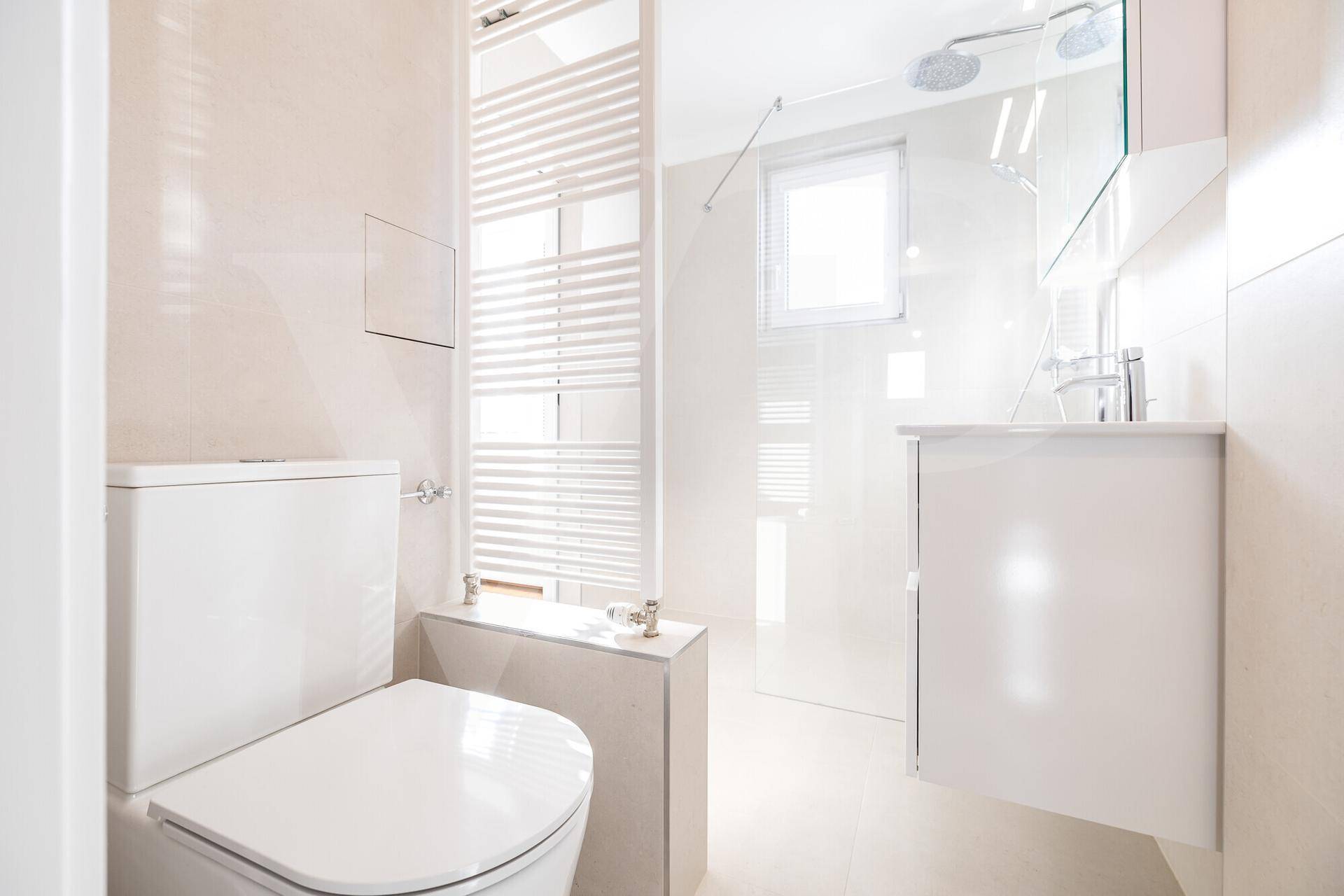 Modernes Badezimmer mit WC, begehbarer Dusche und Waschtisch, hell gefliest.
