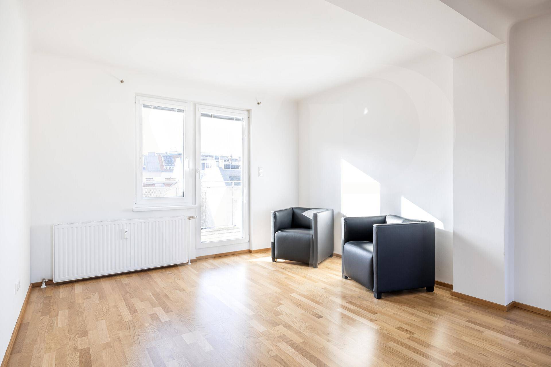 Helles Wohnzimmer mit Parkettboden, zwei Sesseln und großem Fenster mit viel Tageslicht.