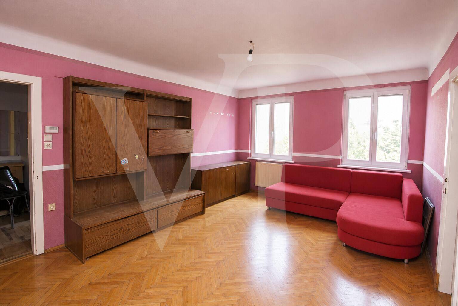 Helles Schlafzimmer mit weiß gestrichenen Wänden, Fischgrätparkett und einem Fenster mit Heizkörper.